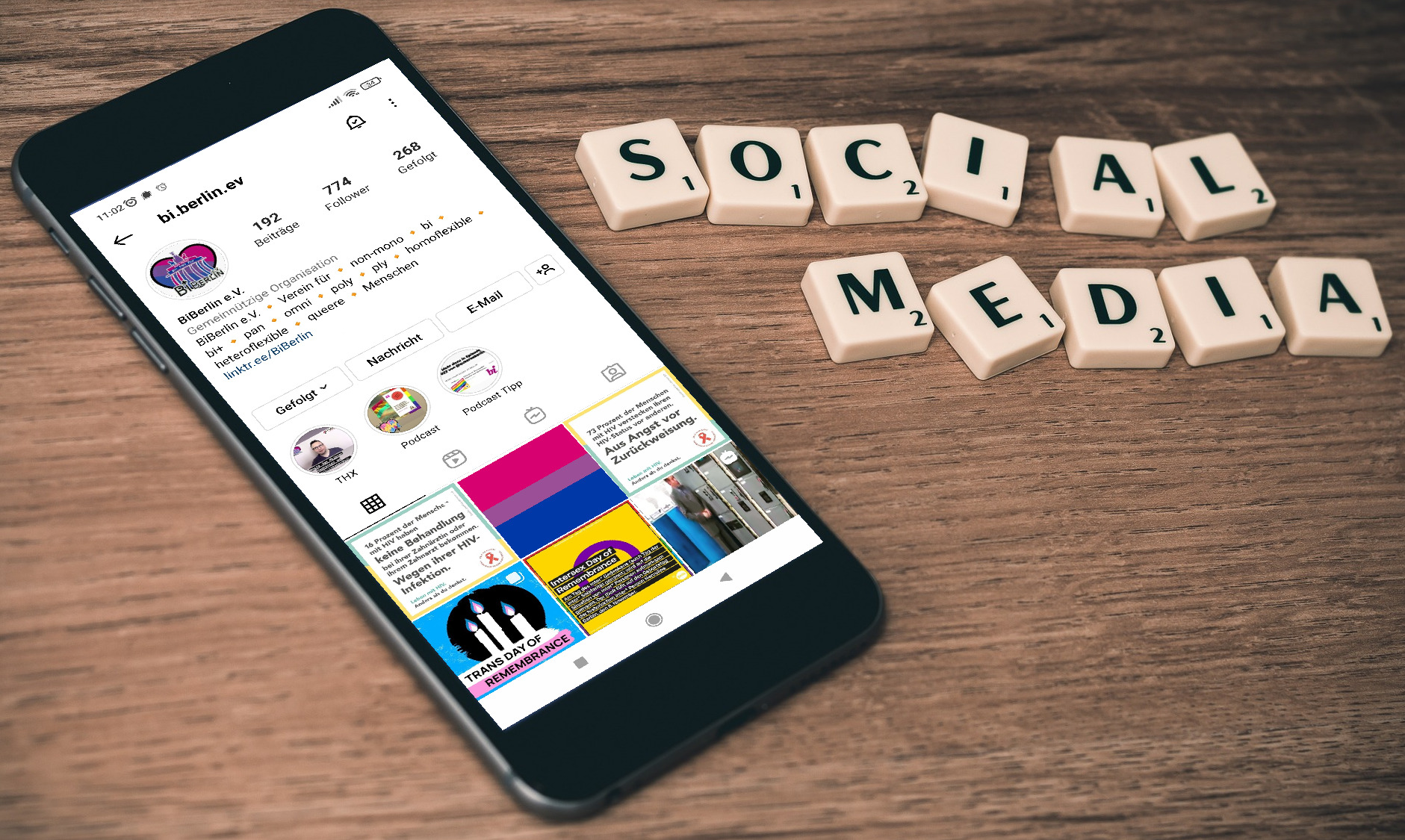 Foto mit Smartphone, auf dem das Instagram-Profil von BiBerlin geöffnet ist. Daneben liegen Buchstabensteine eines Scrabble-Spiels und bilden die Wörter "Social Media"